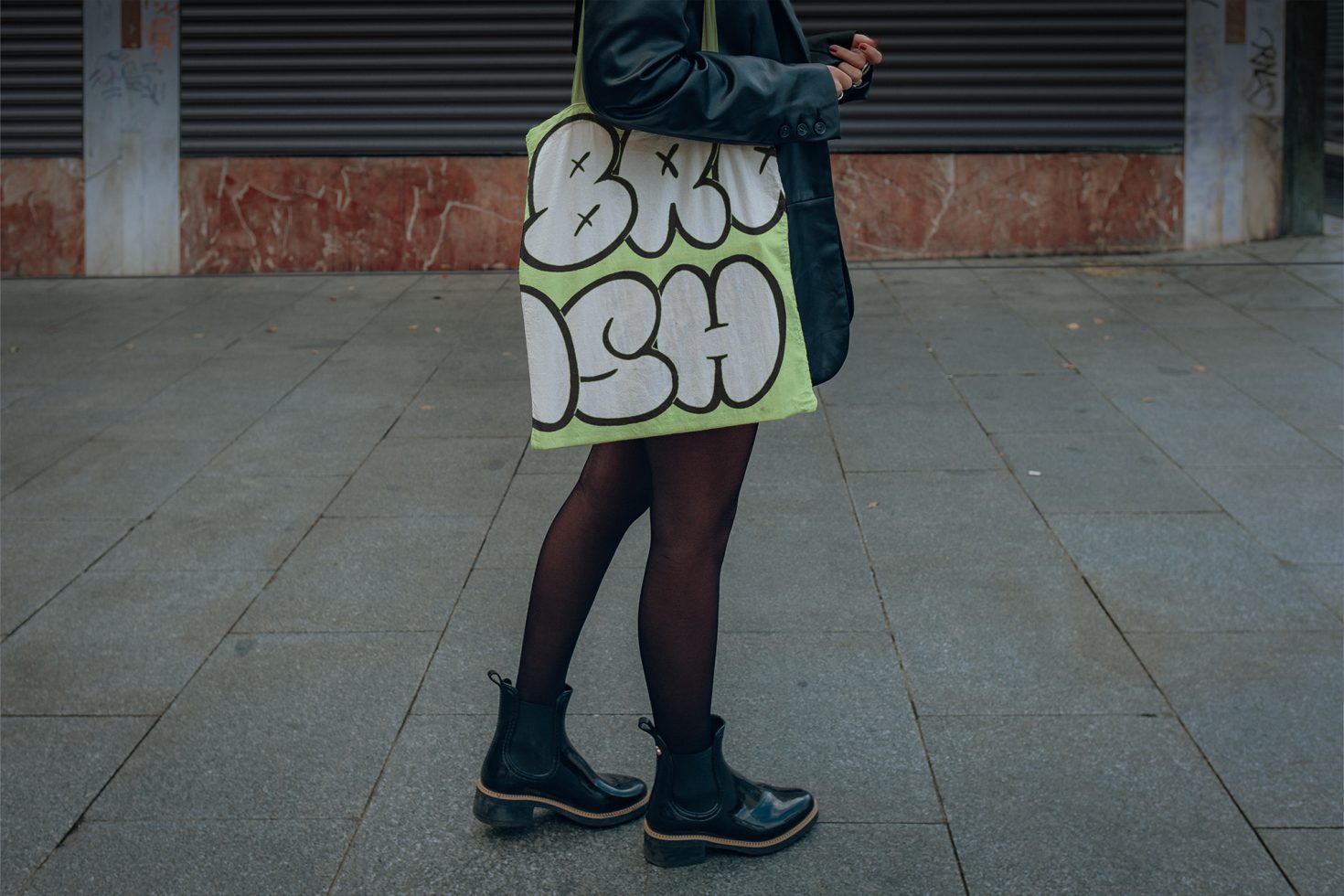 Woman walking street fashion mockup with bold typography on tote bag, urban style, trendy outfit, printed accessories design inspiration.